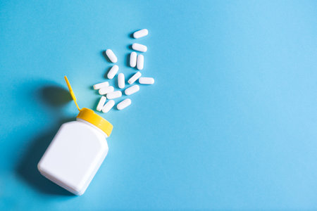 White pills, capsules in plastic bottle on blue background, copy space. Heap of medicine tablets or pills, vitamin and nutritional supplements concept.の写真素材
