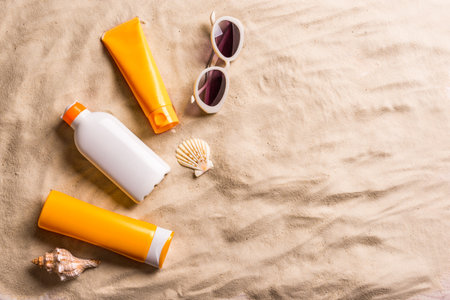 Sunblock lotion bottles, sea shells and sunglasses on sandy beach, copy space. Summer vacation and skin care concept, sunscreen, spf uv-protect cosmetics.の写真素材