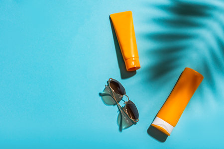 Sunblock lotion bottles and sunglasses on blue background, copy space. Summer vacation and skin care concept, sunscreen, spf uv-protect cosmetics.の写真素材