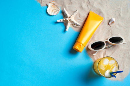 Summer composition with sunblock lotion bottles, starfish, sea shells and sunglasses on blue background with sand, copy space. Summer vacation and skin care concept, spf uv-protect cosmetics.の写真素材