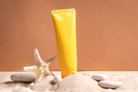 Sunblock in orange cosmetic tube on beach sand and beige background, side view. Summer vacation and skin care concept with starfish and sea shells, spf uv-protect cosmetics.の写真素材