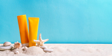 Sunblock lotion bottles, starfish, sea shells and sunglasses on blue background with beach sand, copy space, banner. Summer beach, vacation concept, spf uv-protect cosmetics.の写真素材