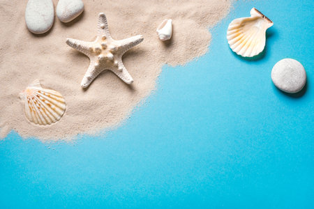 Summer composition with pebbles, starfish and sea shells on blue background with sand, copy space. Summer vacation and beach concept template.の写真素材