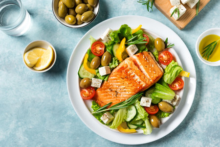 Grilled salmon fish fillet and fresh vegetable salad with tomato, olives, lettuce, feta cheese. Mediterranean keto food - greek salad and roasted salmon on blue background, copy space.の写真素材