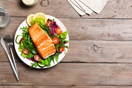Grilled salmon fish fillet and fresh vegetable salad with tomato, lettuce, arugula. Healthy food - green salad and roasted salmon on wooden, top view, copy space.の写真素材