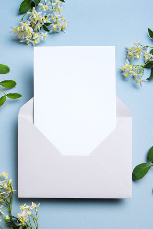 Greeting or invitation blank card in envelope, white delicate clematis flowers on blue gray background, copy space. Stylish creative mock up, romantic date, birthday or holiday celebration concept.の写真素材
