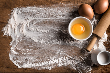 Wheat flour, eggs, rolling pin and whiskey on wooden background, top view, copy space. Ingredients for bakery, baking or cooking concept.の写真素材