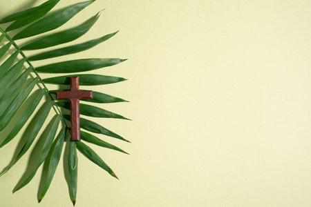 Palm Sunday. Wooden Christian cross and palm leaves on green pastel background, top view, copy space. Palm sunday festival concept.の写真素材