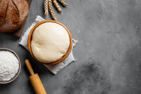Bowl of fresh yeast dough on concrete table, top view, copy space. Raw dough with flour, rolling pin and fresh sourdough bred. Baking and kneading background.の写真素材