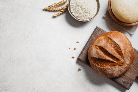 Fresh sourdough bread and ingredients. Loaf of bread on cutting board, ball of dough and flour on...