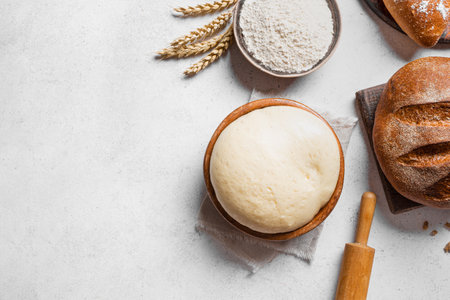 Bowl of fresh yeast dough with flour, rolling pin and fresh sourdough bread on white background, top view, copy space. Baking, pastry and kneading concept.の写真素材