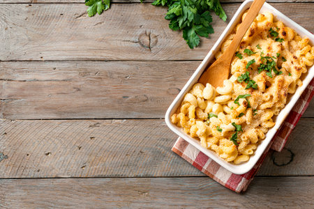 Mac and cheese with breadcrumbs oven baked on wooden background, top view, copy space. Traditional American comfort meal, macaroni pasta and cheese sauce casserole.の写真素材