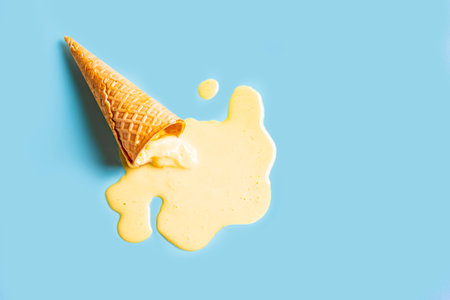 Ice cream waffle cone with melted yellow mango ice cream on pastel blue background. Minimalistic...