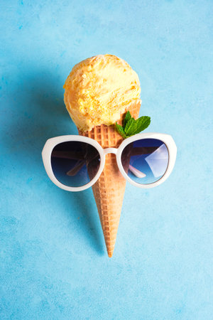 Summer creative concept with yellow ice cream cone and sunglasses on ice blue background. Trendy beach relax and summer vacation theme.の写真素材
