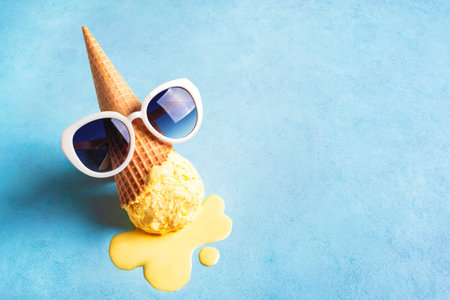 Summer creative concept with melting yellow ice cream cone and sunglasses on blue background, copy space. Trendy beach relax and summer vacation theme.の写真素材