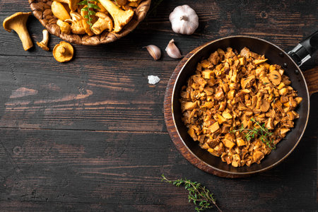 Fried chanterelle mushrooms in pan on dark wooden background, top view, copy space. Forest Mushrooms chanterelles raw and roasted, seasonal local meal.の写真素材