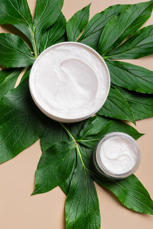 Face cream moisturizer jar and tropical green leaves close up, top view. Natural vegan skin care products, organic anti-aging cream, plant based cosmetic.の写真素材