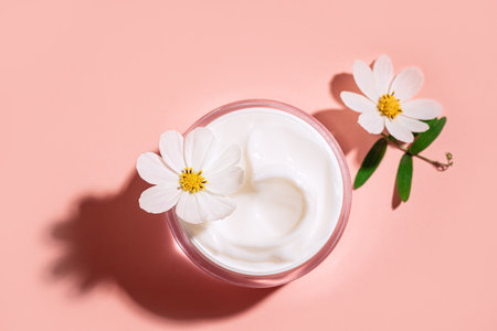 Natural organic cosmetic cream with delicate white flowers on pink background, top view. Collagen beauty cream, anti aging organic skin care concept.の写真素材