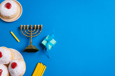 Hanukkah flat lay with golden Menorah, candles, gift box and sufganiyah jelly donuts. Jewish holiday Hanukkah concept design on blue background, top view, copy space.の写真素材