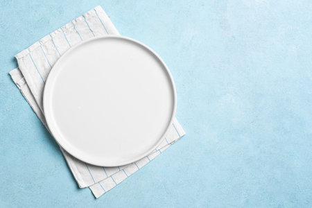 Empty white plate with napkin on light blue background, top view, copy space. Food design template, catering meal menu mock up.の写真素材