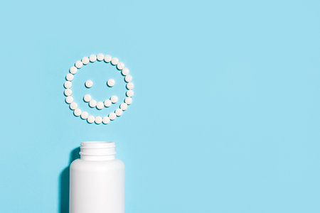 Happy smiling face made of white pills and blank container on blue background, copy space. Smiley from medical pills, creative health care concept.の写真素材
