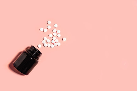 White pills spilling from black container on pink background, minimal concept of health care, top view, copy space. Vitamins and melatonin supplement for healthy sleeping.の写真素材