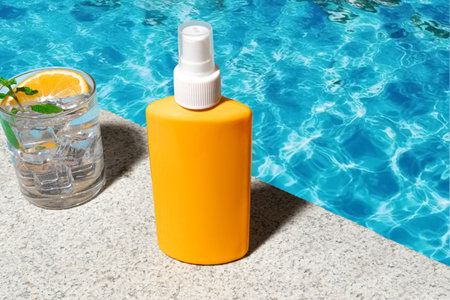 Sunscreen bottle with cocktail drink on stone poolside background near blue pool water background, copy space. Sun protection concept.の写真素材