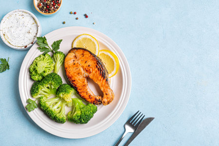 Grilled Salmon fish steak with steamed broccoli vegetables and yogurt sauce on blue background, top view, copy space. Healthy balanced food concept, keto diet.の写真素材