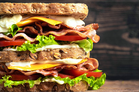 Double BLT sandwich with cheddar cheese on dark wooden background, extremely close up. Healthy lunch sandwich with wholegrain bread, bacon, lettuce, tomato, cheese and sauce.の写真素材