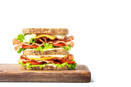 Double BLT sandwich with cheddar cheese on wooden board isolated on white background, design element. Healthy lunch sandwich with wholegrain bread, bacon, lettuce, tomato, cheese and sauce.の写真素材