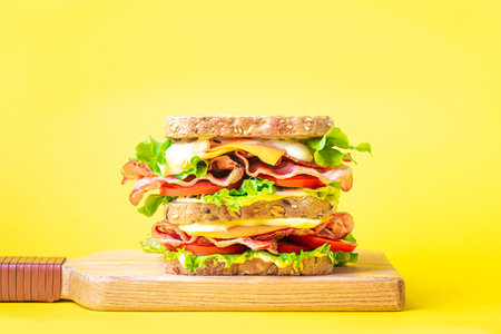 Double BLT sandwich with cheddar cheese on bright yellow background, creative design. Healthy lunch sandwich with wholegrain bread, bacon, lettuce, tomato, cheese and sauce.の写真素材