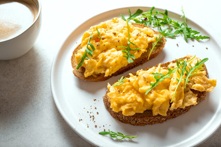 Scrambled Eggs on wholegrain bread toasts with arugula and cup of coffee close up. Healthy keto breakfast.の写真素材