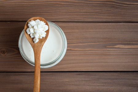 Milk kefir grains on wooden spoon and jar of kefir, top view, copy space. Preparing healthy homemade fermented probiotic milk kefir drink.の写真素材