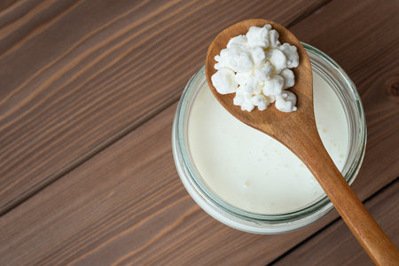 Milk kefir grains on wooden spoon and jar of kefir on wooden table, top view, copy space. Preparing healthy homemade fermented probiotic milk kefir drink.の写真素材