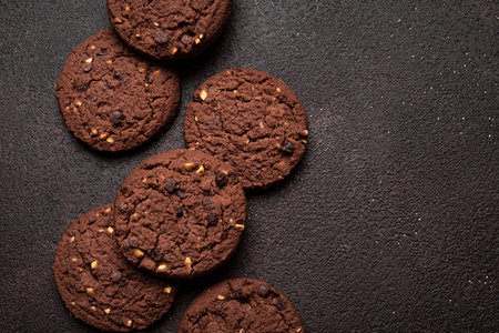 Chocolate chip cookies with hazelnuts on dark brown background, top view, copy space. Texture of...