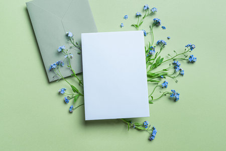 Greeting or invitation 5x7 card design, empty blank card with envelope and floral decor on green background, copy space for text. Creative mockup with wild delicate blue forger-me-not flowers.の写真素材