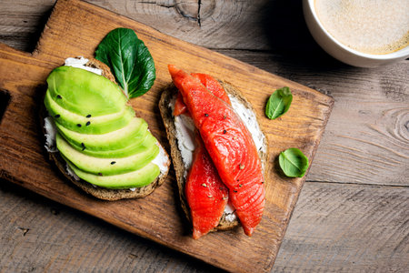 Avocado and salmon toast with cream cheese and greens, top view. Healthy breakfast open sandwiches with salmon and avocado on wooden background.の写真素材