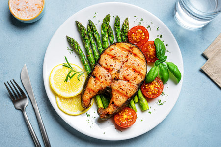Grilled salmon steak with green asparagus, tomatoes and lemon slices on blue background, top view. Balanced healthy meal, keto lunch.の写真素材