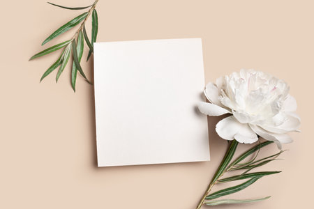 Greeting or invitation card mockup, white empty blank 1x1 with floral decor on neutral beige background, copy space for text. Creative elegant mock up with white peony flower and eucaliptus leaves.の写真素材