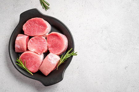 Uncooked pork tenderloin meat medallions ready to cook on white background with rosemary, top view, copy space. Fresh juicy meat pieces, food concept.の写真素材
