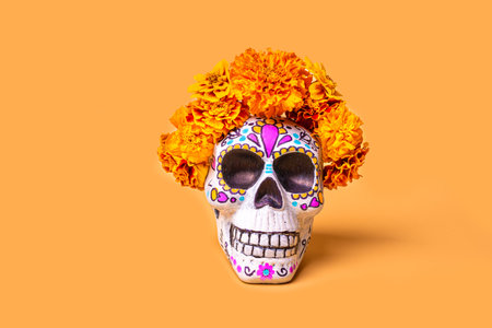 Painted skull for Day of the Dead celebration with marigold flowers on orange background, copy...