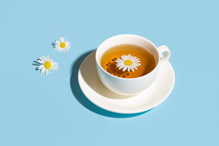 Chamomile tea cup with chamomile flowers on blue background with trendy hard light, copy space. Cup of healthy herbal tea with daisy, minimal design template.の写真素材
