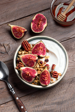 Granola bowl with figs and pecan nuts on wooden background, top view. Healthy breakfast bowl with...