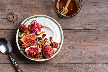 Granola bowl with figs and pecan nuts on wooden background, top view, copy space. Breakfast bowl with Greek yogurt, granola, honey, fruits and nuts.の写真素材