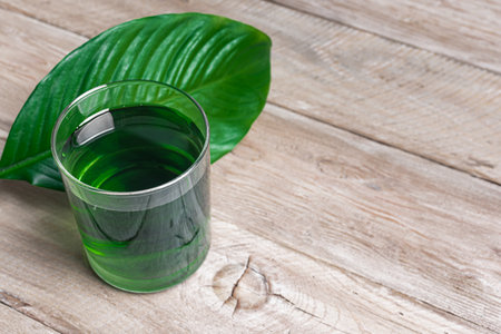 Liquid Chlorophyll Drink. Glass of Chrorophyll Water on wooden table with green leaf, copy space. Healthy eating, clean lifestyle, detox supplement concept.の写真素材