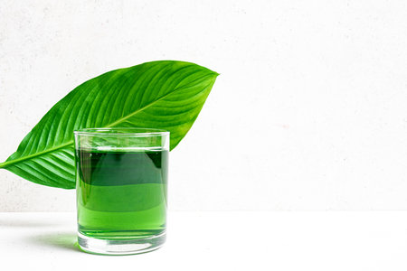Liquid Green Chlorophyll Drink. Glass of Chrorophyll Water on white background with green leaf, copy space. Healthy eating, clean lifestyle, detox supplement concept.の写真素材