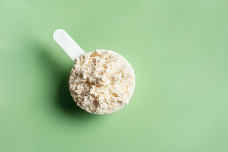 Scoop of whey protein powder on green background, closeup, copy space.