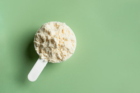 Scoop of whey protein powder on green background, closeup, copy space.の写真素材