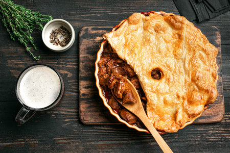 Beef steak pie with dark gravy and crispy puff pastry on rustic wooden background, top view....