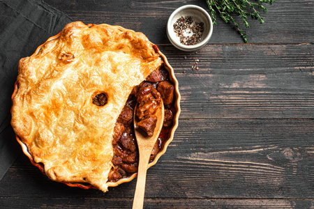 Beef steak pie with crispy puff pastry on wooden background, top view, copy space. Homemade meat pie recipe, comfort food.の写真素材